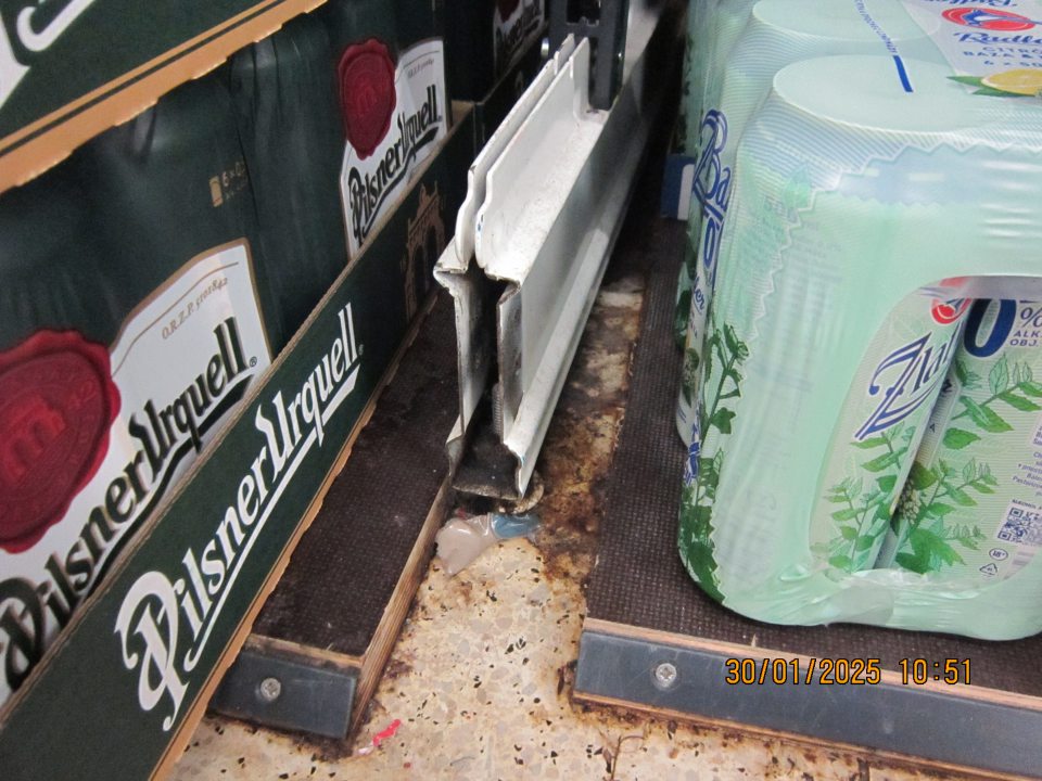 Podlaha znečistená nánosmi čiernej špiny v priestore medzi regálmi s fľašovaným a v plechovkách baleným pivom na predajnej ploche prevádzky. 