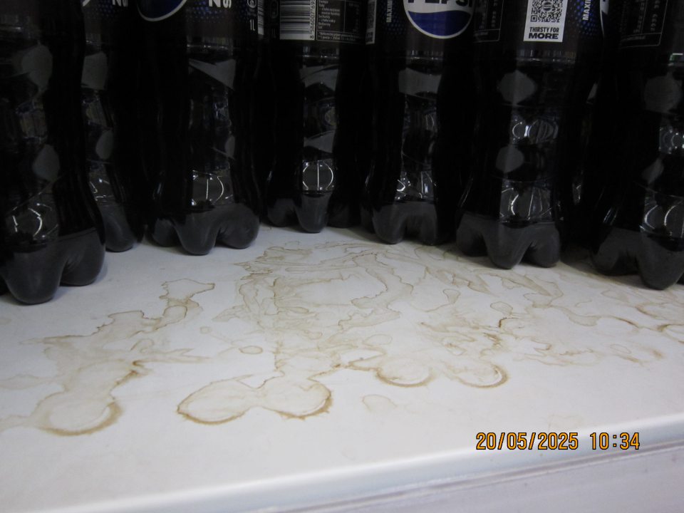 Znečistený regál na uchovávanie pepsi nápojov na predajnej ploche zaschnutými nečistotami z vytečeného obsahu.