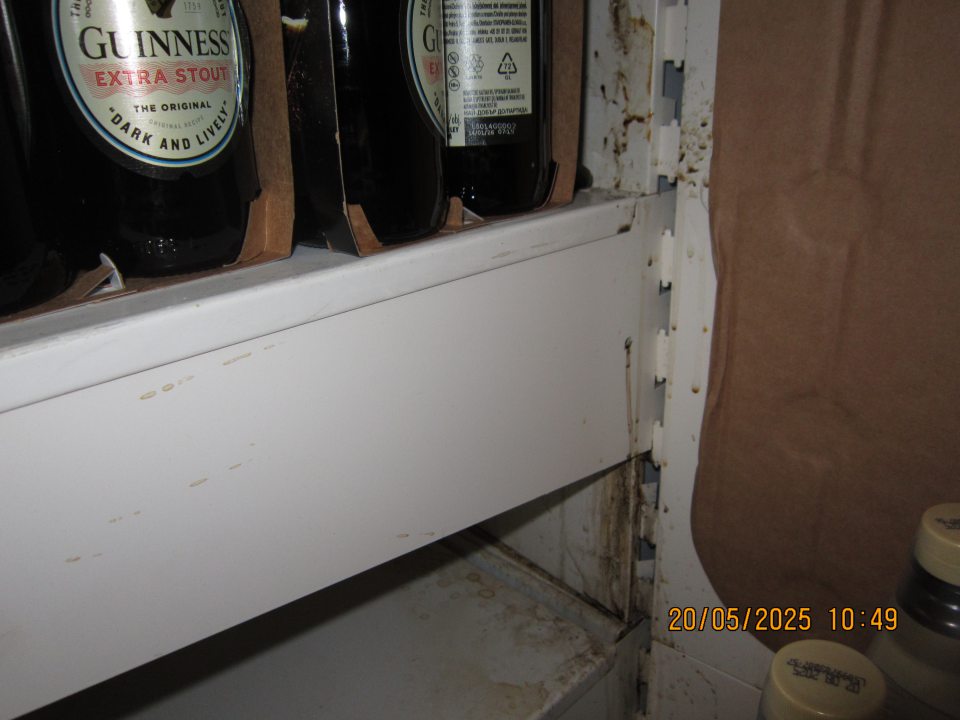 Znečistený regál na uchovávanie pív vo fľašiach a plechovkách na predajnej ploche zaschnutými nečistotami z vytečeného obsahu.