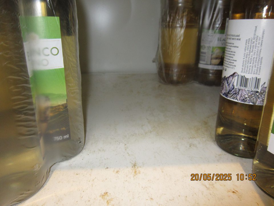 Znečistený regál na uchovávanie alkoholických nápojov-vín na predajnej ploche zaschnutými nečistotami z vytečeného obsahu.