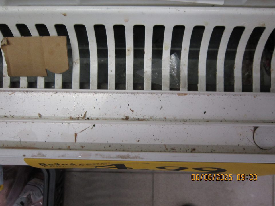 Silne znečistené mriežky, priestor pod mriežkami a  drážky zasúvacích dvierok v chladiarenskej vitríne na uchovávanie chladeného mäsa– prach, drobné nečistoty a útržky kartónov.