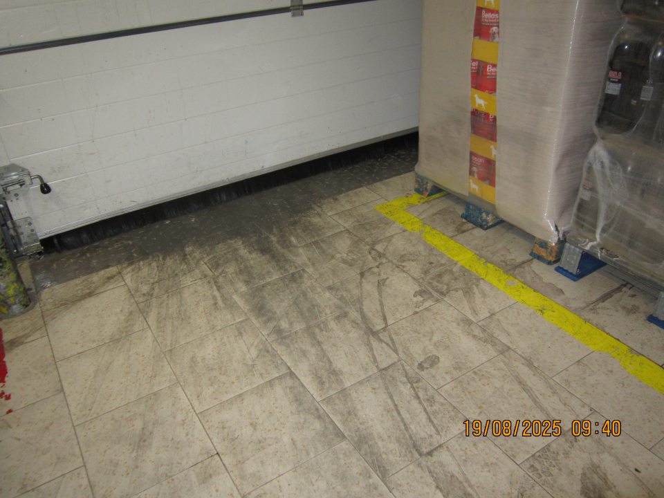 Vrstva čiernej špiny nalepená na podlahe v okolí príjmovej rampy v  skladovacej časti prevádzky.