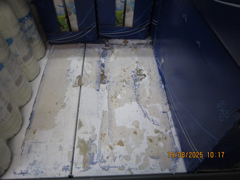 Zaschnutými nečistotami a prilepenými kúskami kartónového papiera   znečistený regál v chladiacej vitríne na uchovávanie čerstvého mlieka na predajnej ploche prevádzky.