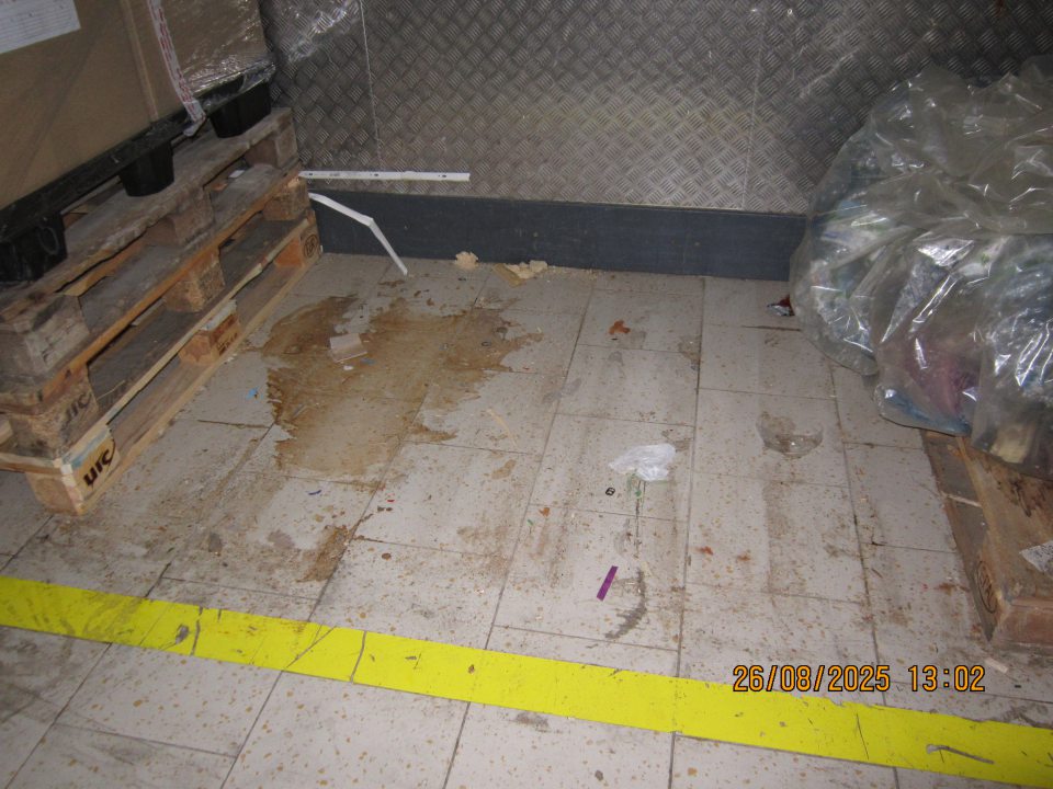 Rozliata tekutina a nečistoty na podlahe pri paletách s návratnými plastovými obalmi v skladovacej časti prevádzky.