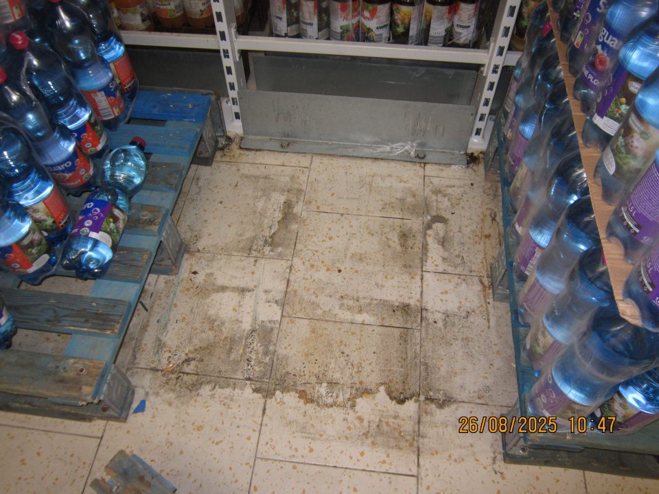 Znečistená podlaha medzi paletami s balenou minerálnou vodou na predajnej ploche prevádzky.