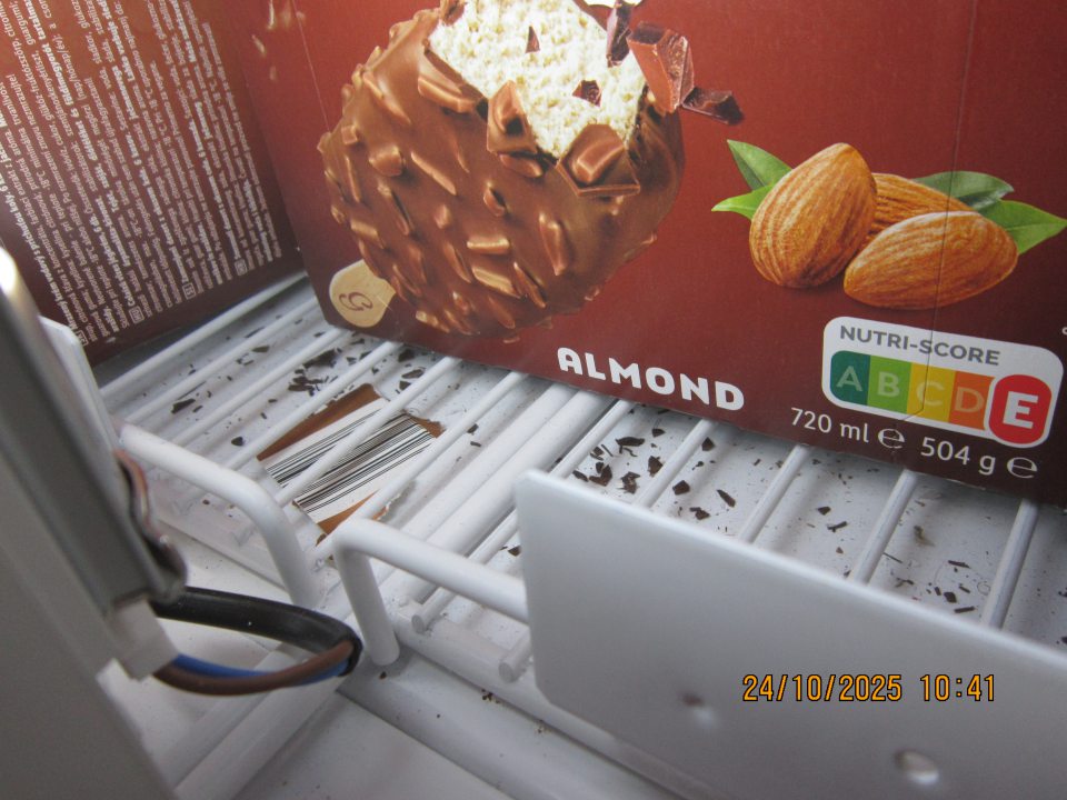 Znečistená spodná časť pod mriežkou v mraziacej vitríne slúžiacej na uchovávanie mrazených krémov organickými nečistotami – kúsky čokolády,  útržkami kartónu.