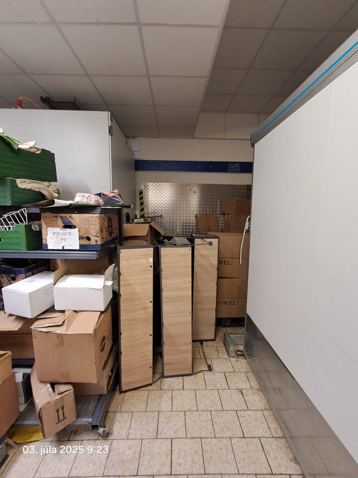 Väčšie množstvo kartónových krabíc, nepoužívaného inventáru a ďalších predmetov v rohu v sklade potravín.