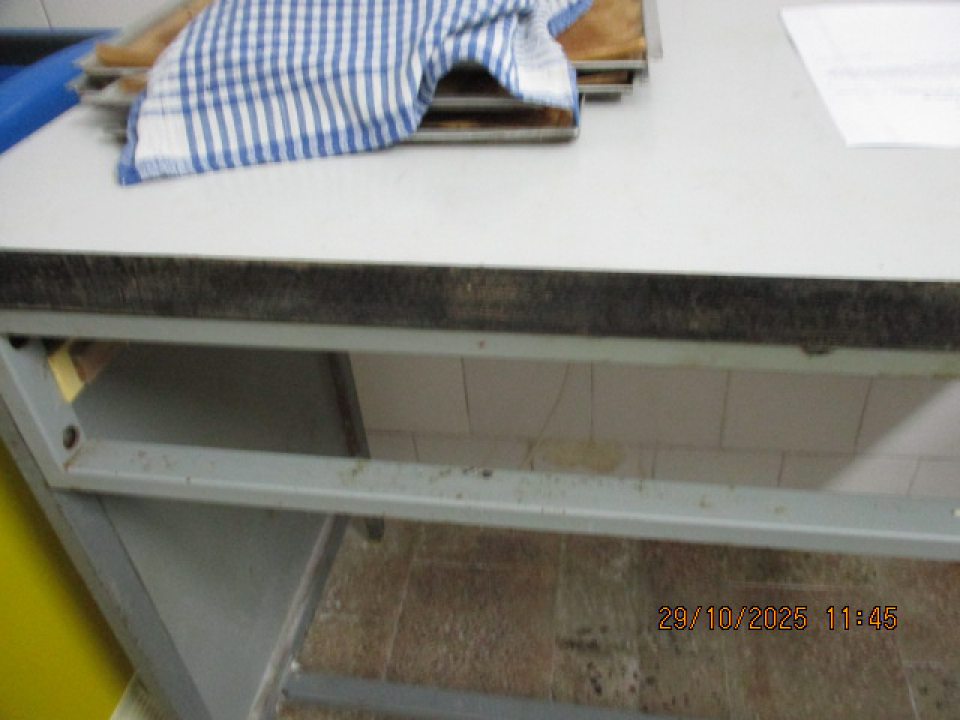 Pracovný stôl využívaný na manipuláciu s polotovarmi pri procese dopekania pekárskych výrobkov má opotrebovanú kovovú konštrukciu,bočná kovová lišta znečistená nánosom zvyškov múky.