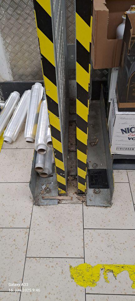 V suchom sklade potravín podlaha v okolí oporných kovových stĺpov znečistená hrubou vrstvou nečistoty, prachu, papierikmi, úlomkami dreva.