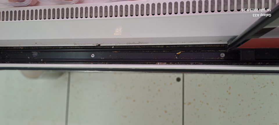 Chladiaca vitrína na mäso je v drážkach posuvných dvierok znečistená hrubou nečistotou, zasušenými zvyškami potravín.