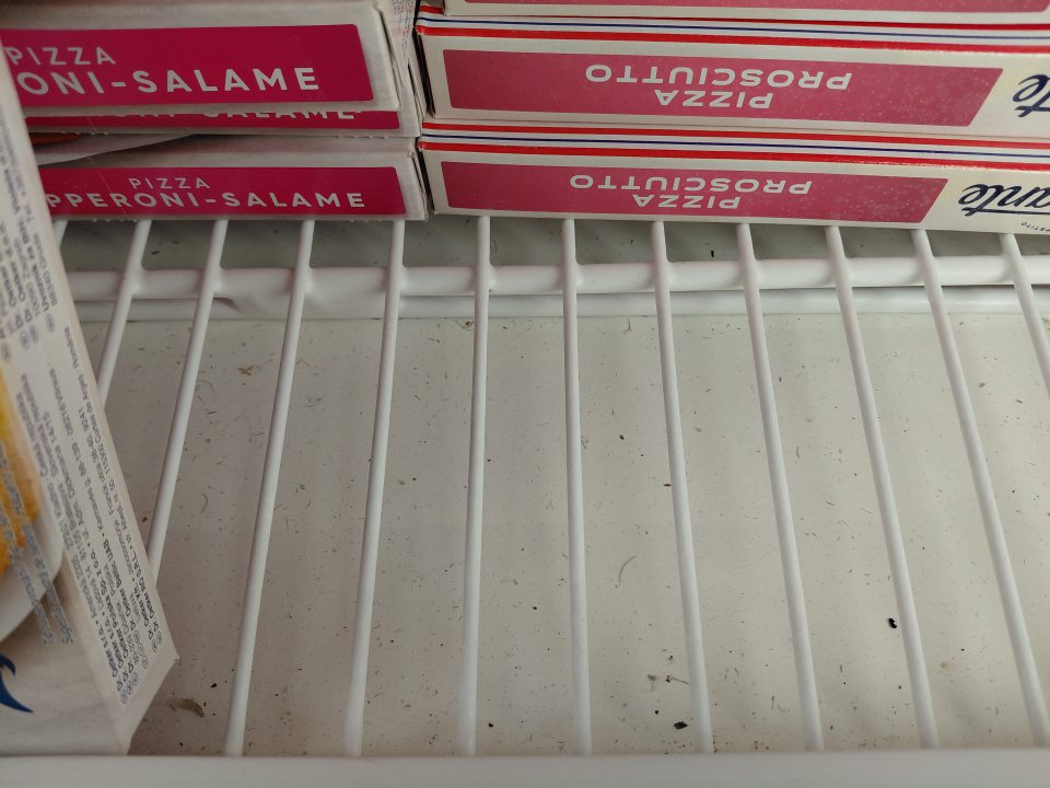 Mraziaci box - polica pod mrazenými pizzami znečistená prachom, nečistotami, omrvinkami