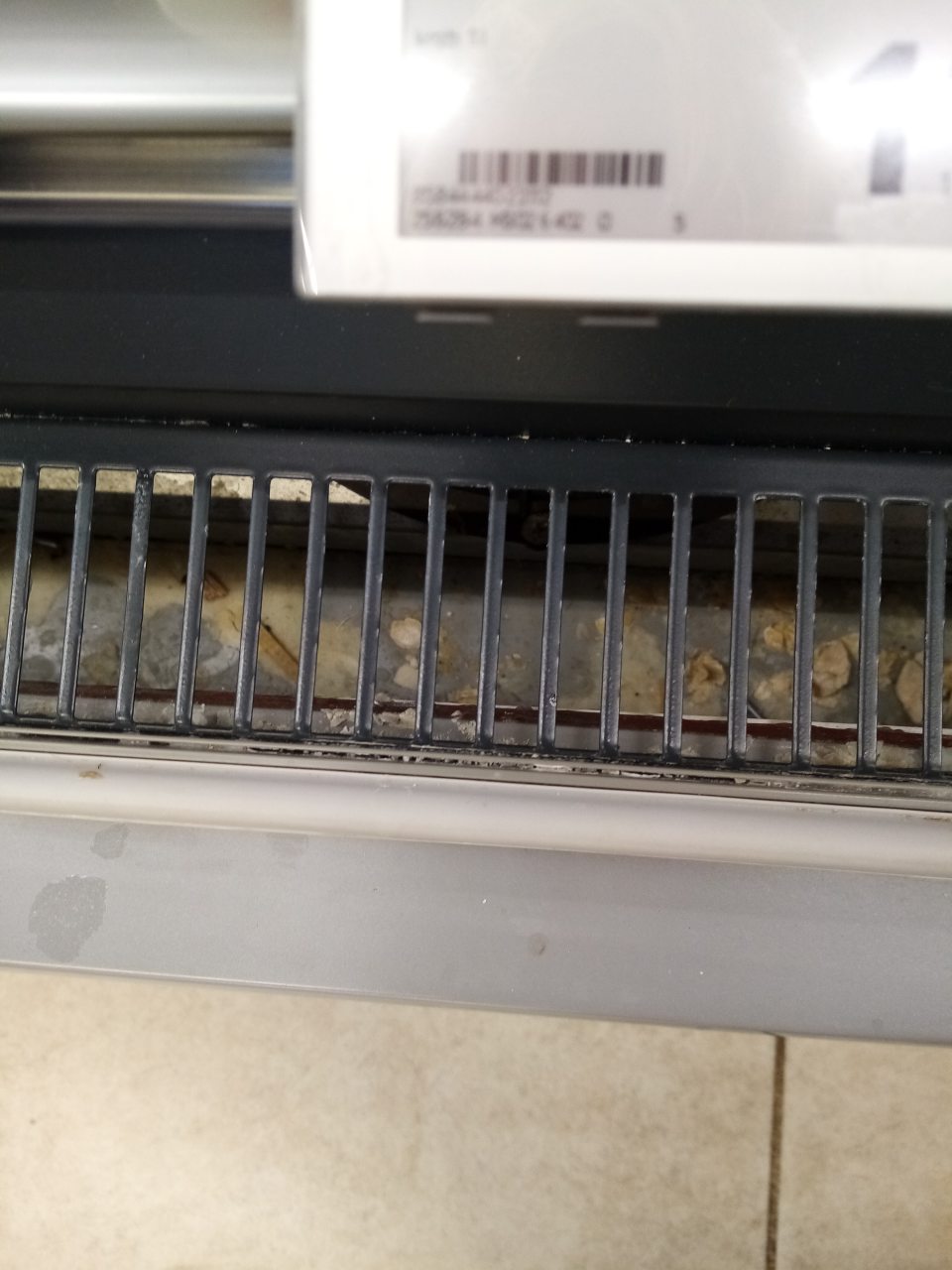 Znečistený priestor pod mriežkou v chladiacej vitríne určenej na predaj mliečnych výrobkov.