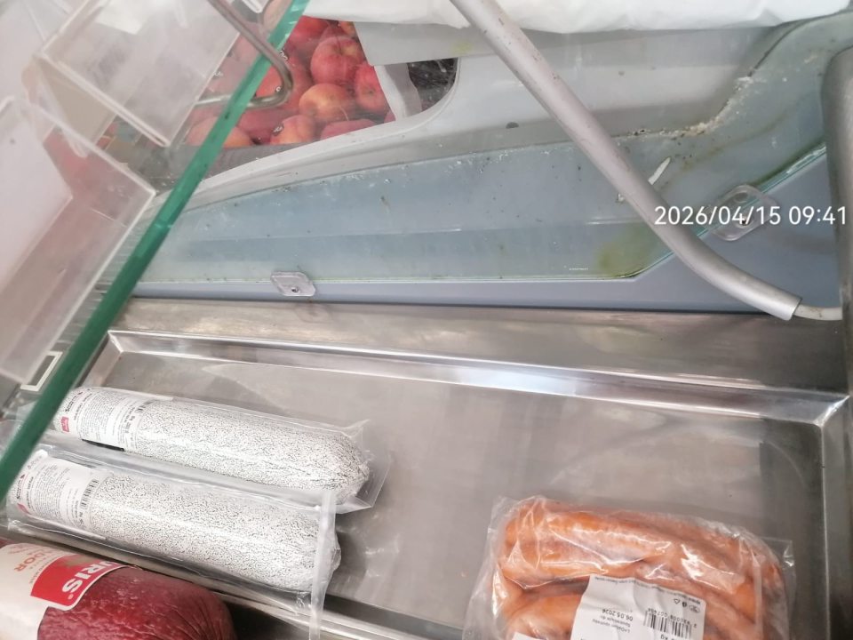 Znečistený priestor medzi sklom a konštrukciou na chladiarenskej vitríne s mňsovými výrobkami mechanickými nečistotami.