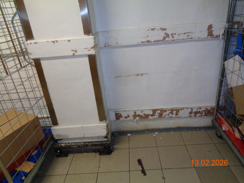 V skladovacej časti prevádzky v priestore umiestnenia kovových klietok s tovarom poškodená stena a protinárazové drevené lišty s olupujúcim sa náterom.