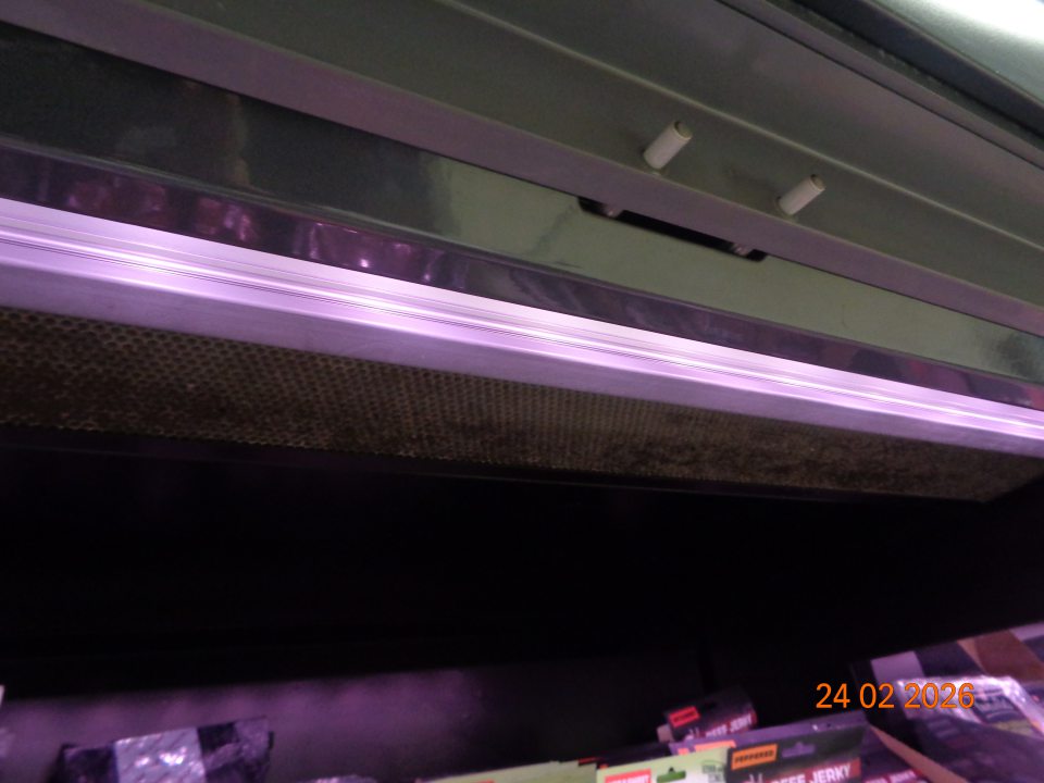 Silne znečistená mriežka v hornej časti chladiarenského zariadenia na uchovávanie trvanlivých mäsových výrobkov na predajnej ploche súvislou vrstvou čiernej špiny a prachu.