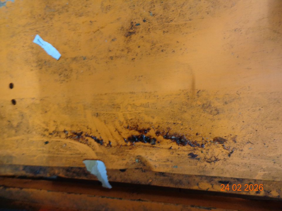 Silne znečistená úložná plocha kovového paletizačného zariadenia z distribučného centra čiernou špinou a zaschnutým vytečeným obsahom z uloženého tovaru.