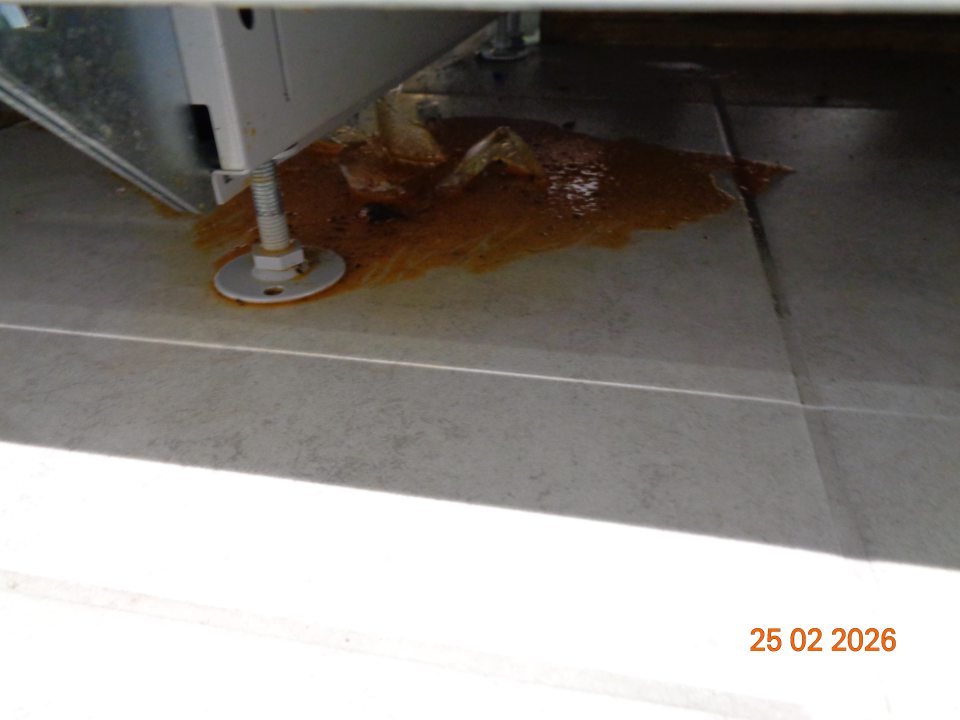 Zaschnutý vytečený obsah nápojov a plastový obalový materiál na podlahe pod regálom  so sirupmi, džúsmi a ochutenými nápojmi na predajnej ploche prevádzky.