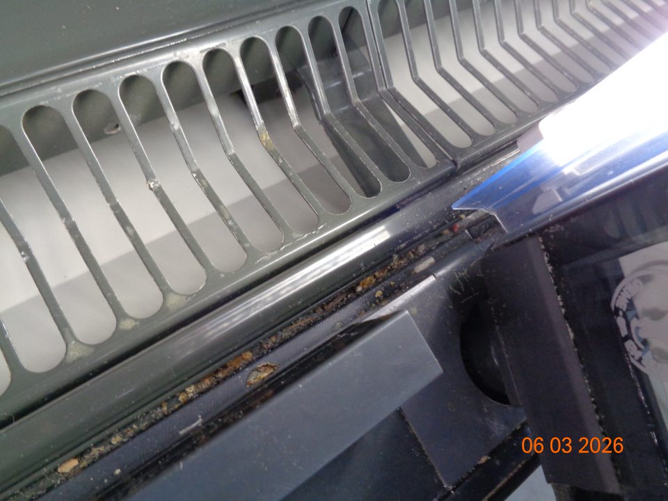 Znečistené priestory medzi mriežkami a kovovými rámami organickými nečistotami, špinou a prachom v dolnej časti chladiaceho zariadenia na uchovávanie mäsových výrobkov.