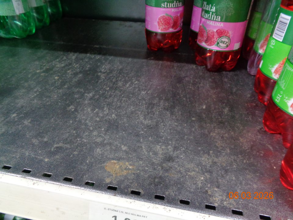 Znečistený regál na uchovávanie nealkoholických ochutených nápojov zaschnutou špinou a prachom.