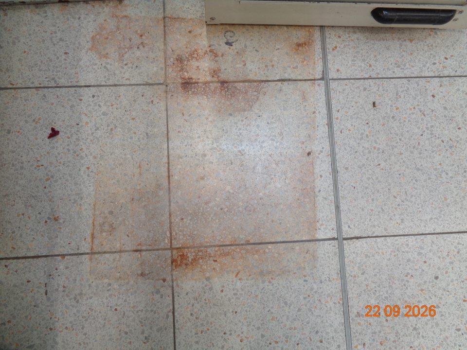 Hrdzavou škvrnou znečistená podlaha pri pokladni na predajnej ploche.
