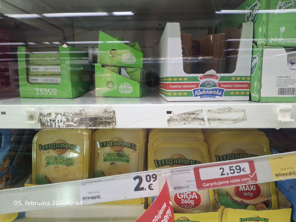 Na predajnej ploche znečistený regál v chladiacom zariadení na mliečne výrobky pod lištou na cenovky čiernymi nečistotami.